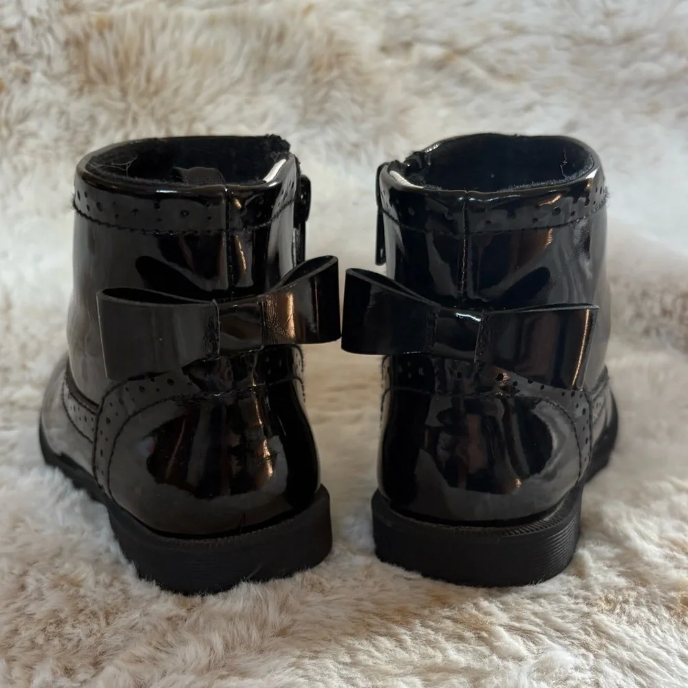 Little girls glossy black boots with bow on the back.